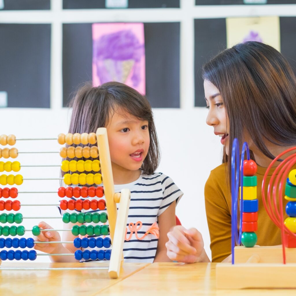 Asian female teacher teaching mixed race kids play toy