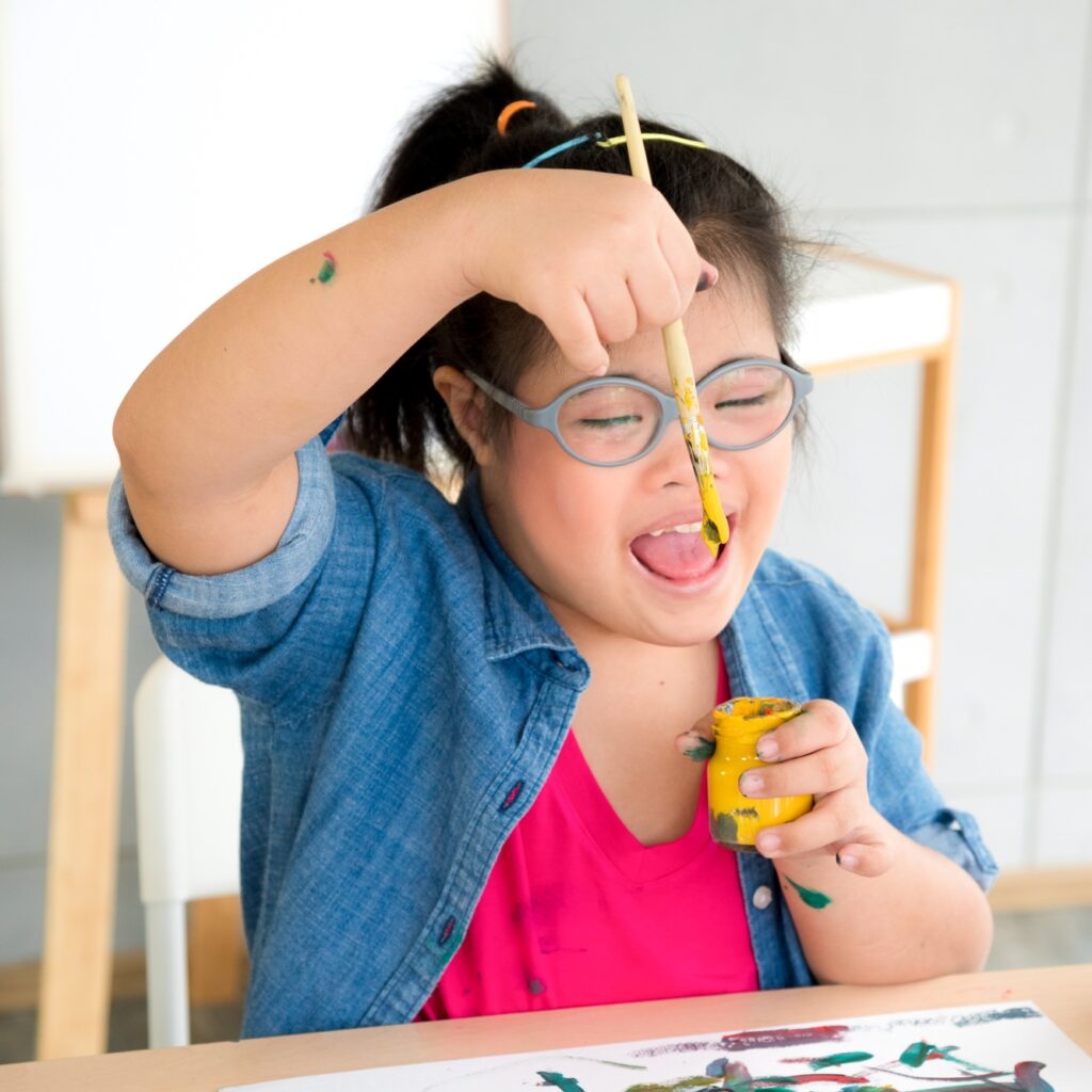 Young autism disabled child complex genetic disorders kid drawing a picture by watercolor.